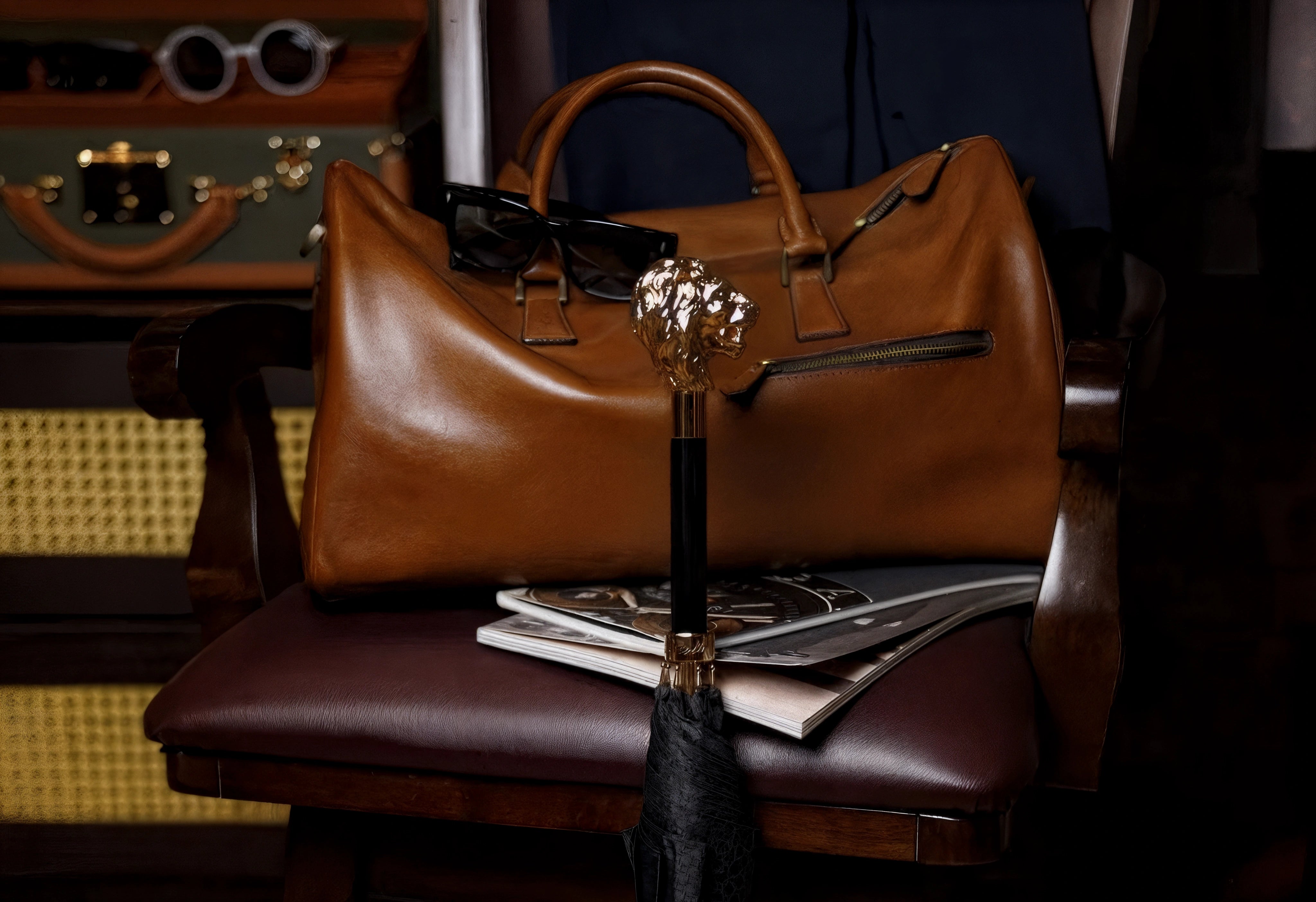 Brown leather handbag on a chair with sunglasses and a newspaper underneath, in a room with vintage suitcases.