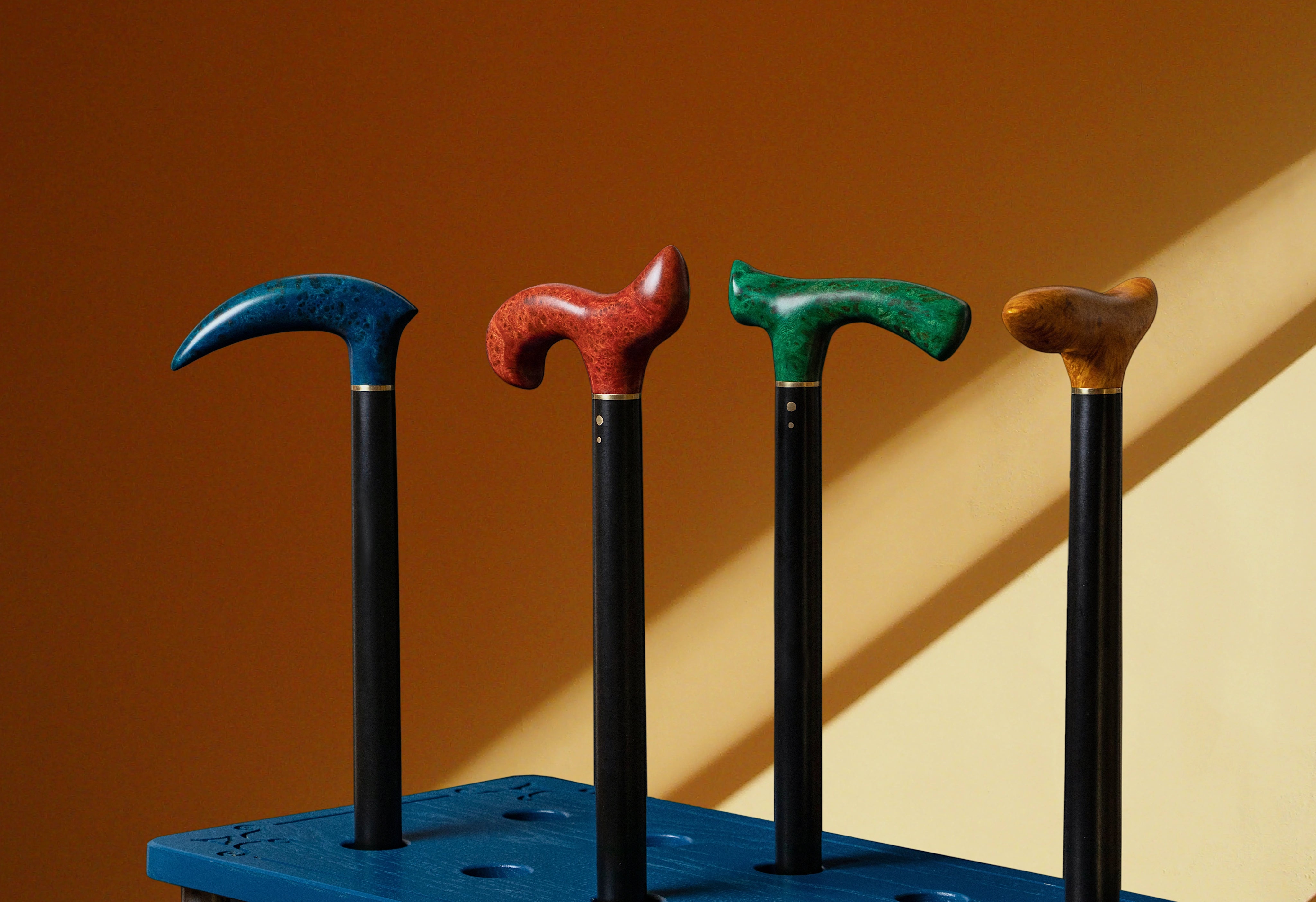 Four walking sticks with different colored handles on a blue stand against a brown and beige background.